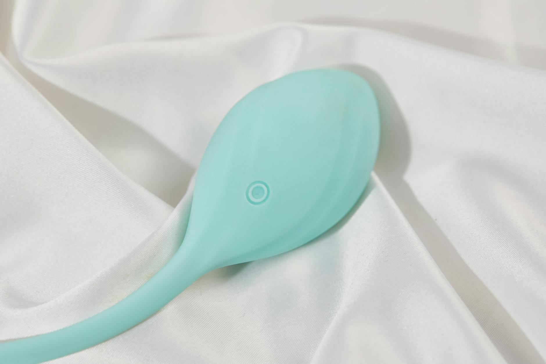 A stylish teal air suction vibrator on white silk, representing modern pleasure technology