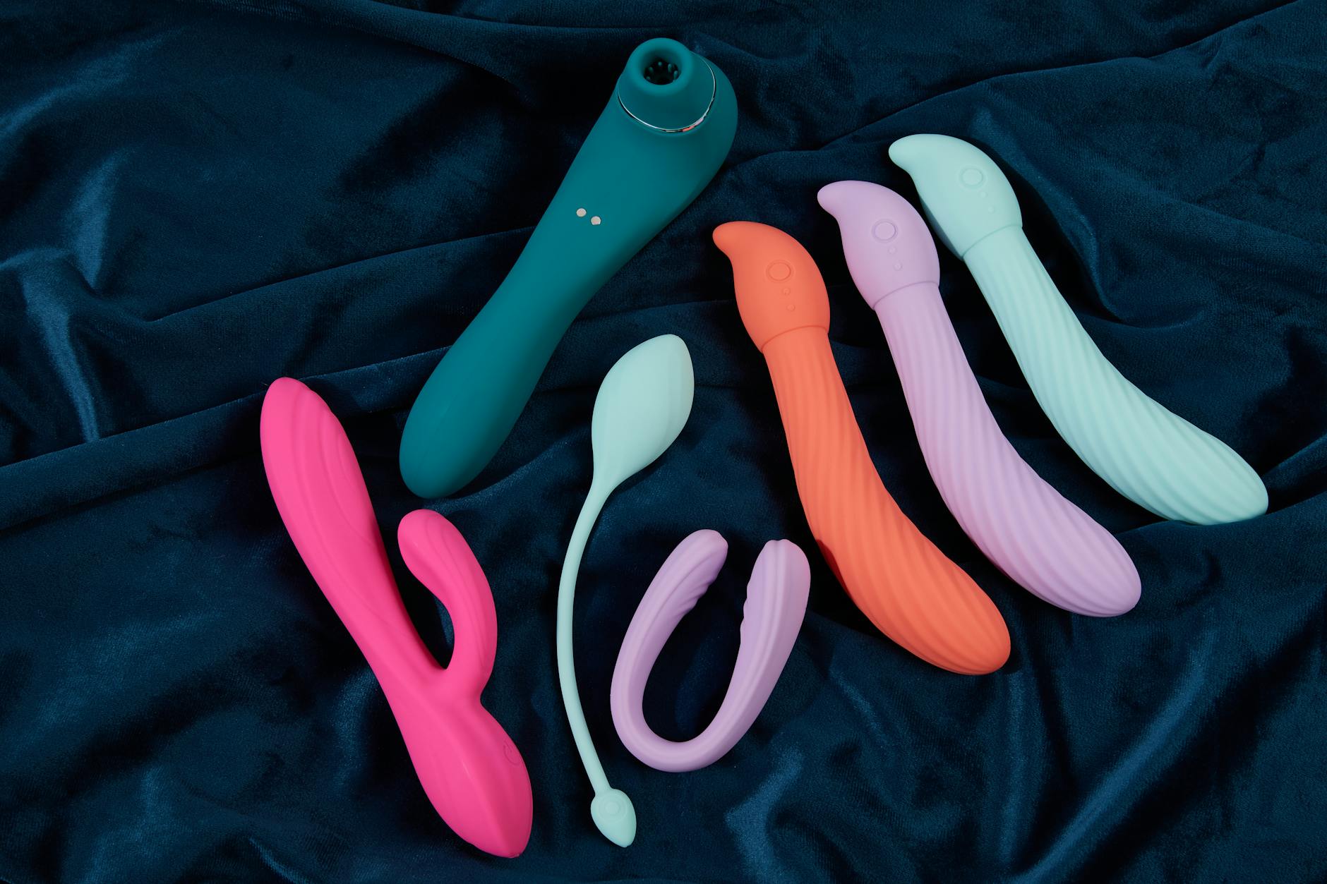A teal clitoral vibrator resting on smooth white silk fabric