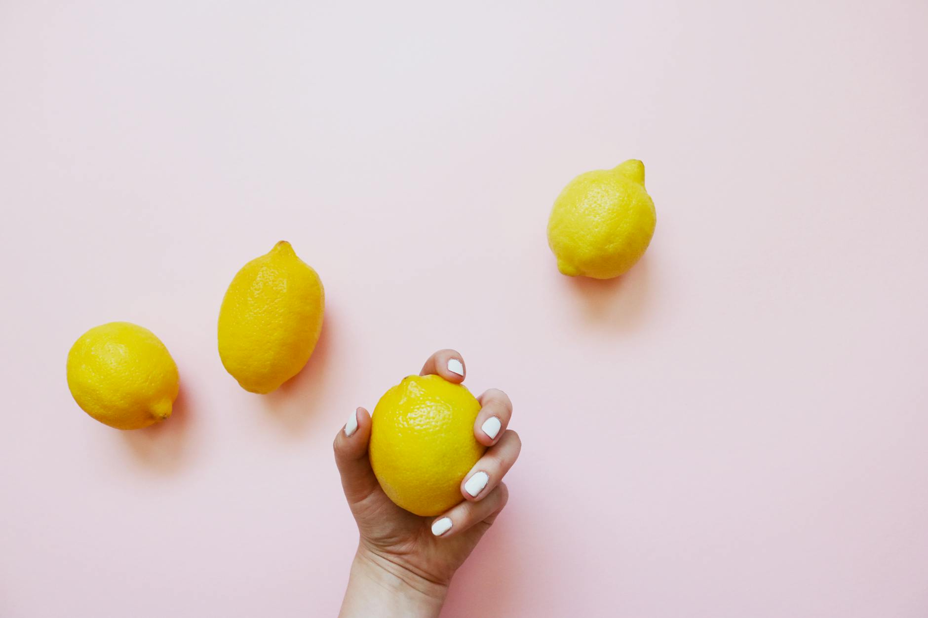 A hand holding a fresh lemon on a soft pink background, representing fresh approaches to pleasure