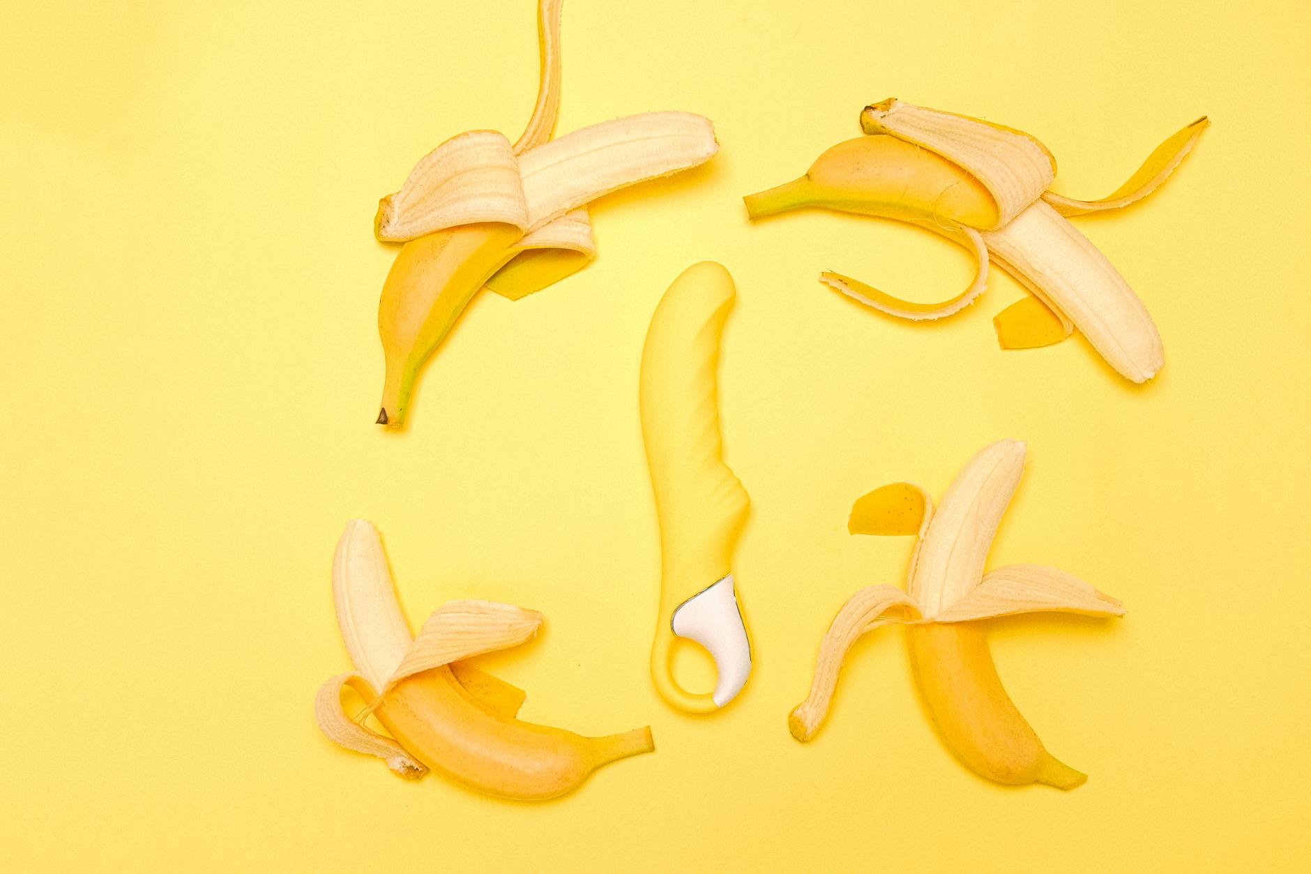 Vibromasseur jaune en silicone entouré de bananes pelées sur fond jaune