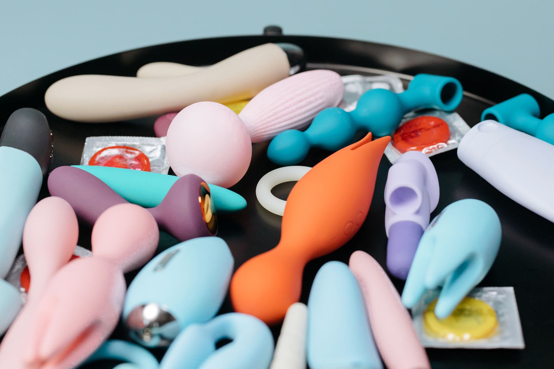 A collection of colorful vibrators and intimate wellness tools arranged on a dark surface