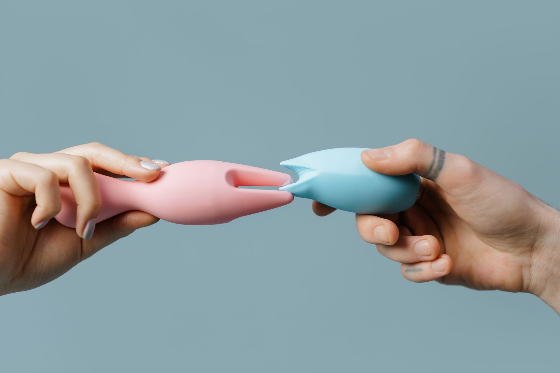 Woman holding blue and pink silicone vibrators in a contemplative manner