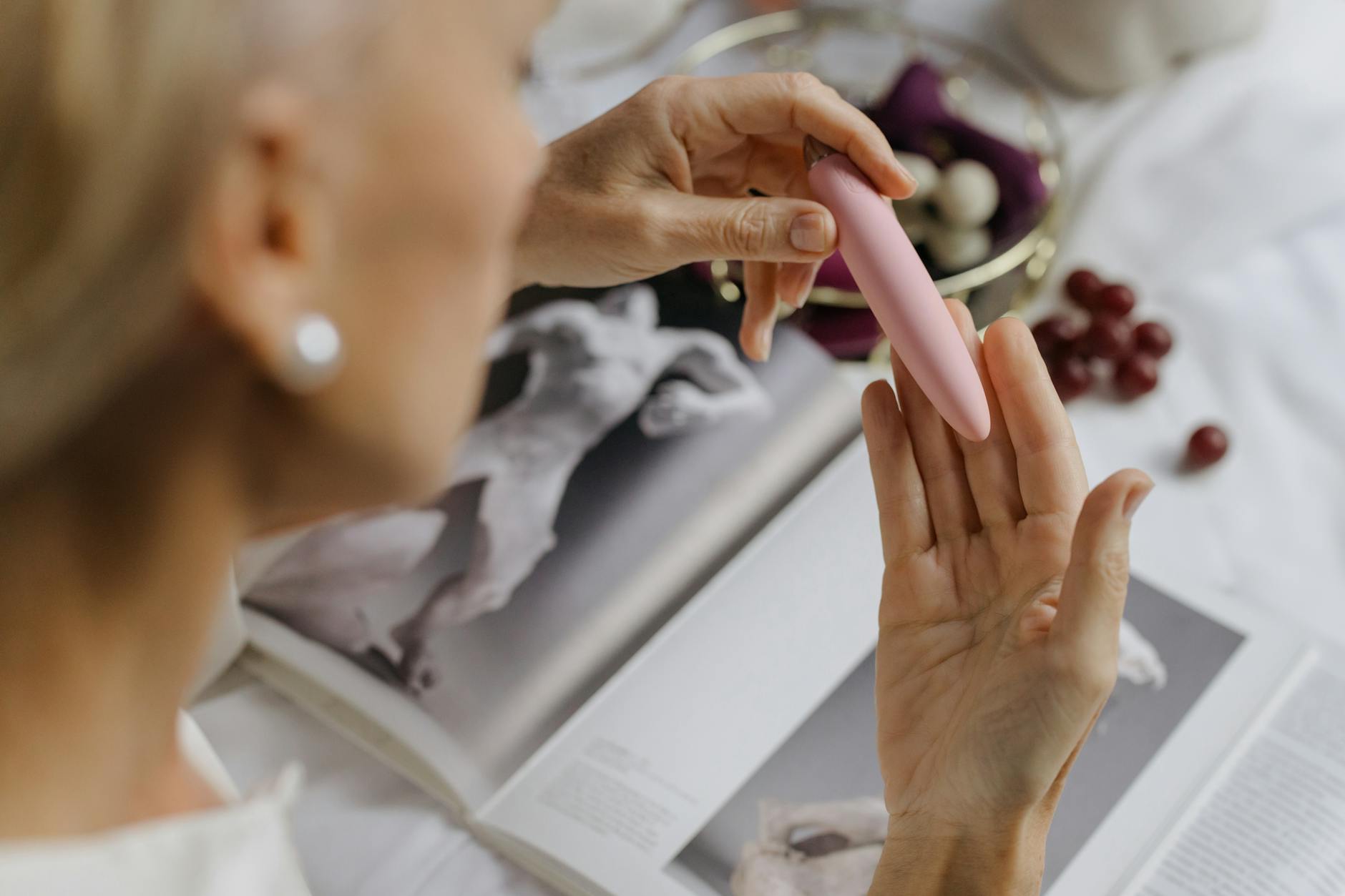 Gros plan d'une femme tenant un vibromasseur rose avec des livres d'art en arrière-plan, mettant l'accent sur les thèmes intimes et personnels.