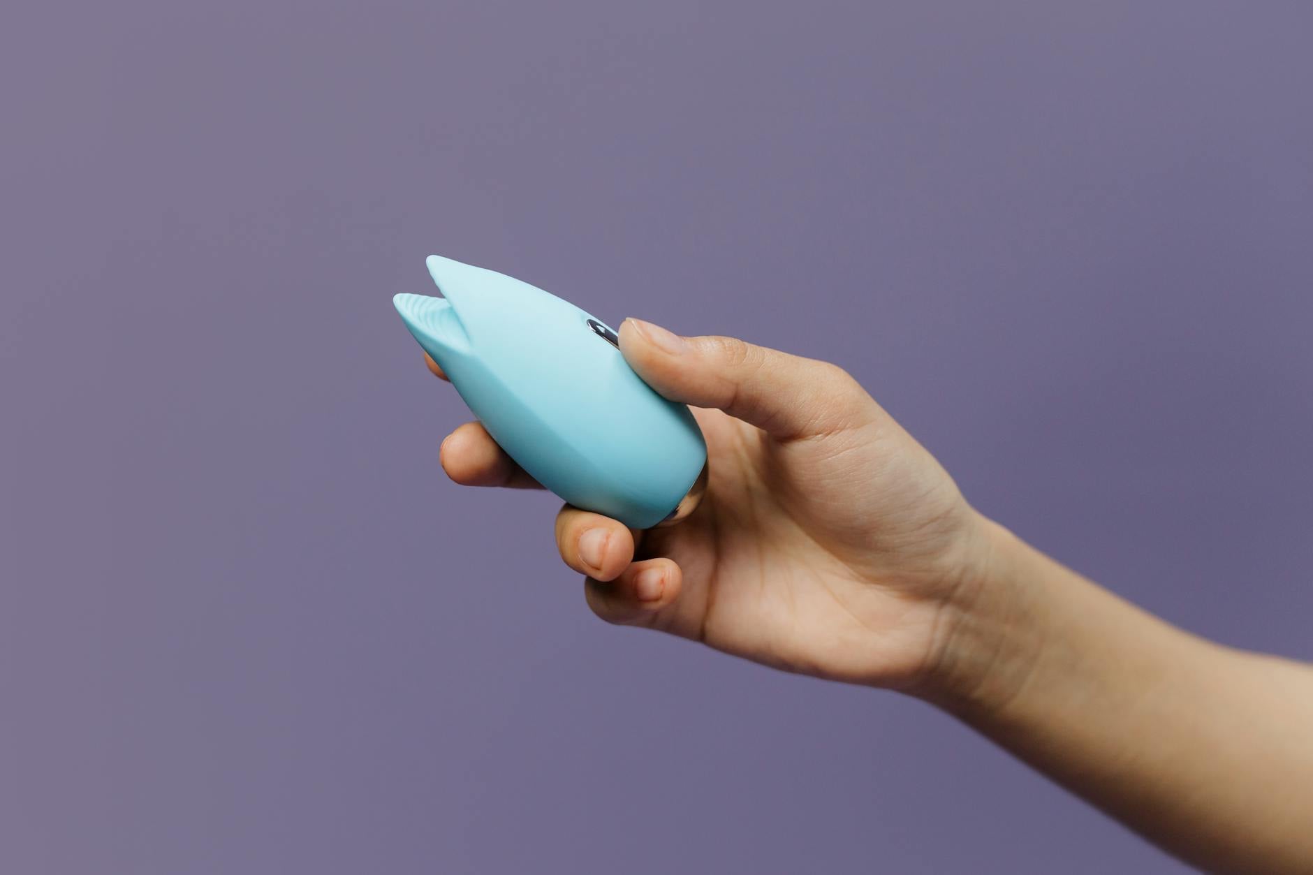 Hands holding a blue silicone vibrator against a purple background