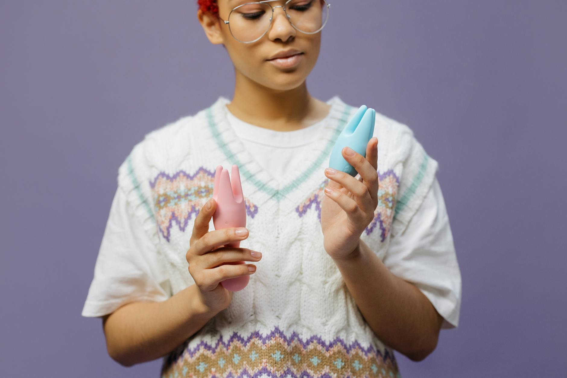 A person holding blue and pink silicone vibrators in a thoughtful pose, representing options for pelvic health and pleasure.