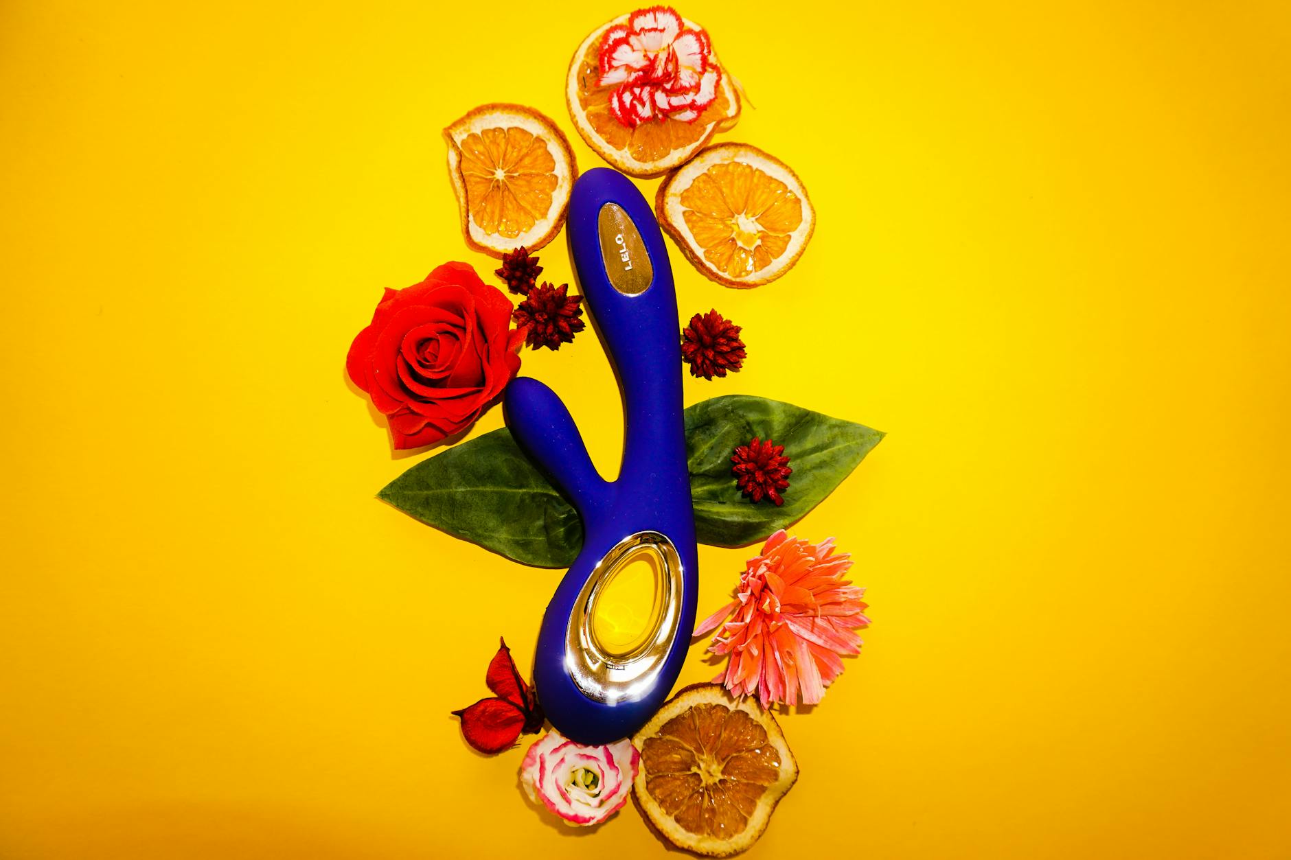 A blue lemon clitoral vibrator surrounded by fresh lemons and orange slices on a bright yellow background.